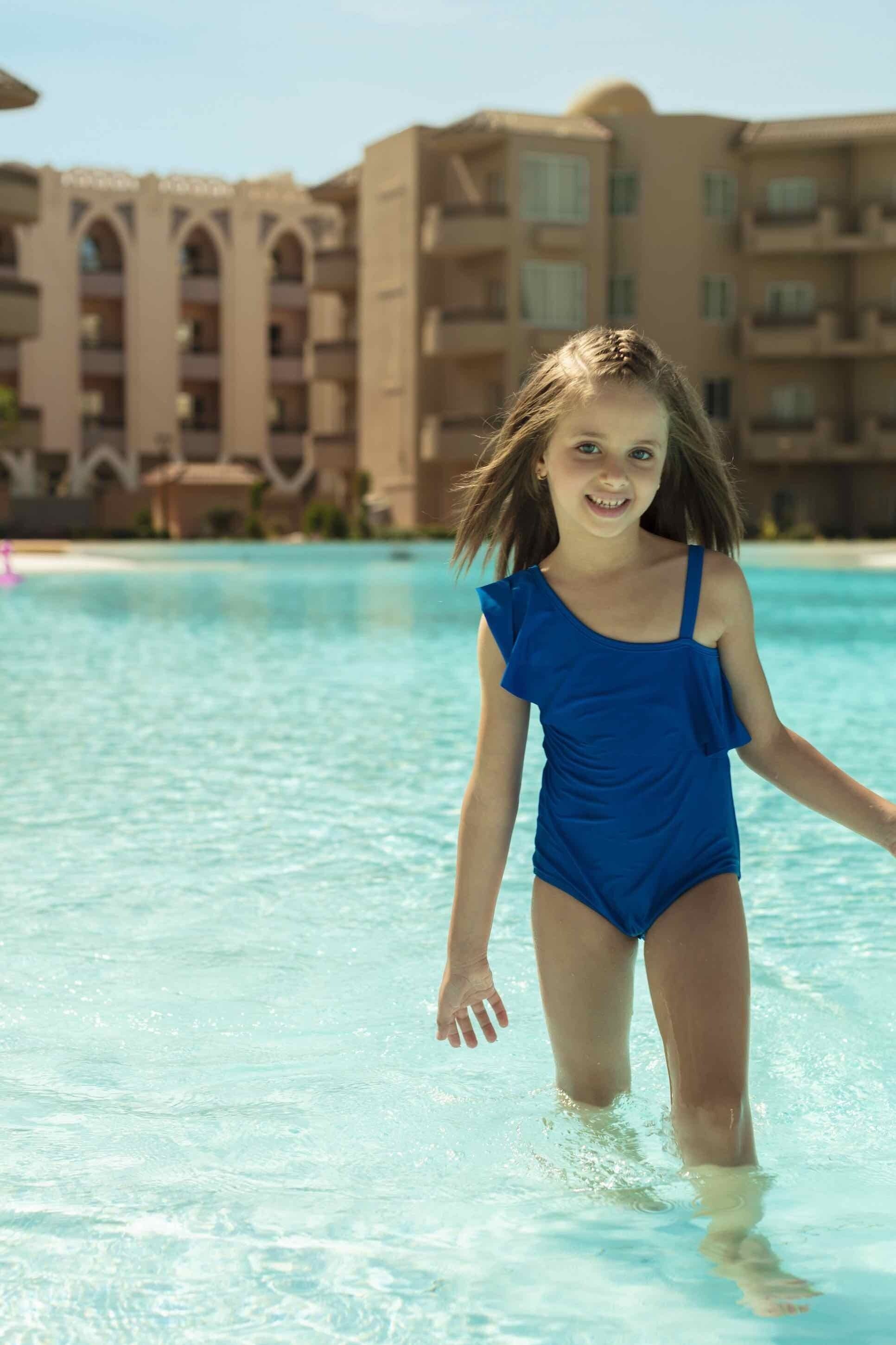 En person i blå badetøj står i en pool med en hotelbygning i baggrunden.