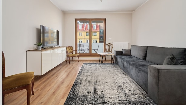 Un salon moderne avec un canapé, un téléviseur, une table à manger et une vue dégagée sur l’extérieur grâce à une grande fenêtre.