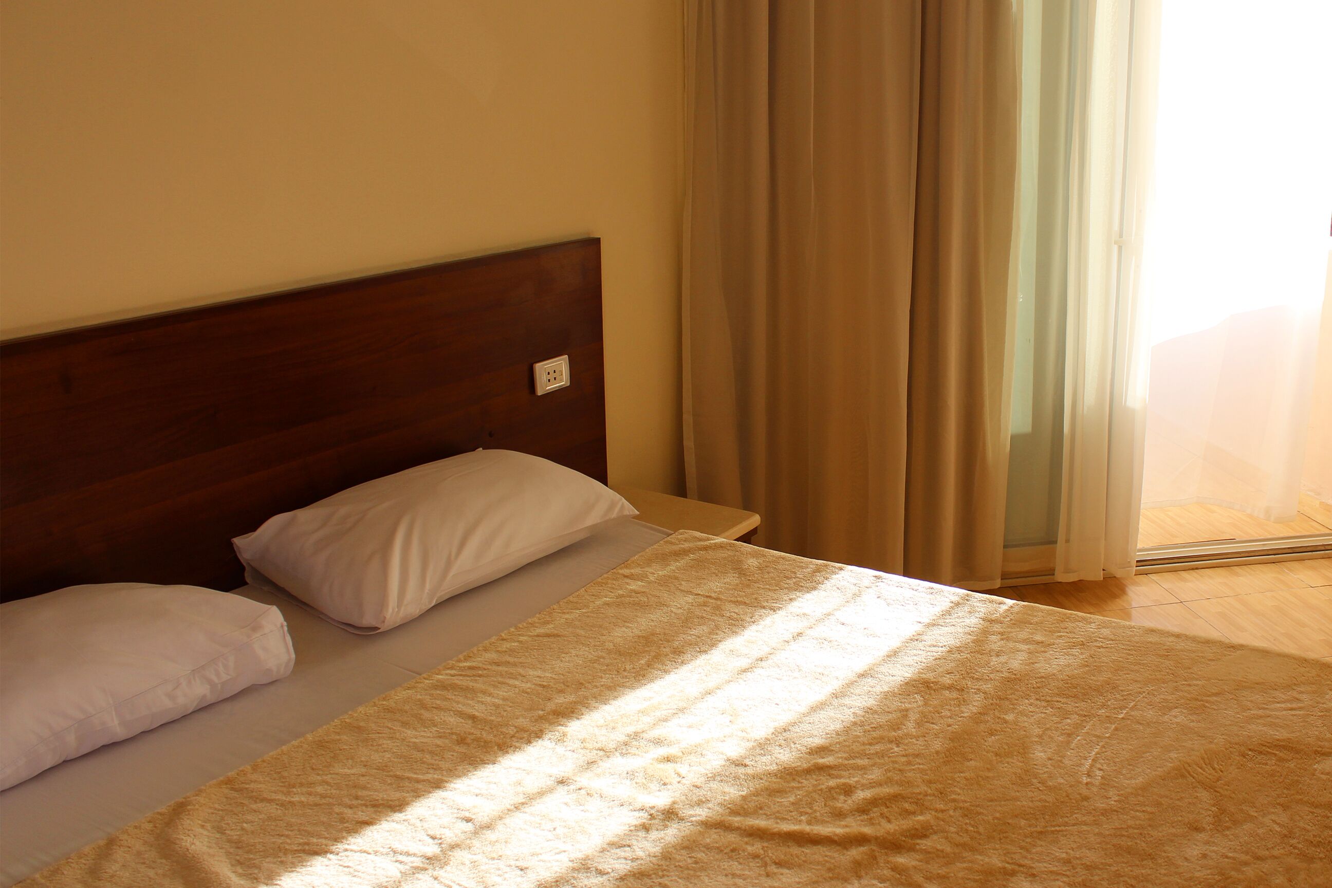 Cama com cabeceira de madeira, almofadas brancas e manta bege.