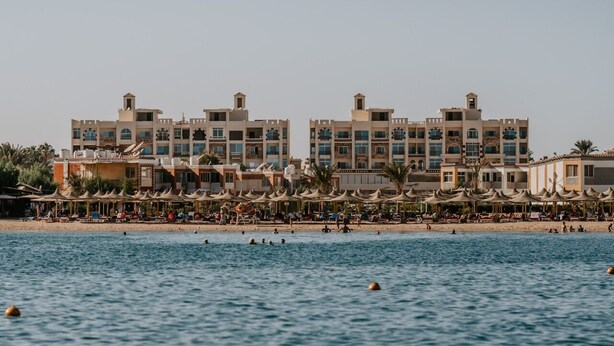 Un hotel frente a la playa con varias edificaciones, una playa de arena y sombrillas.