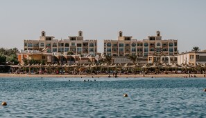 Hotel à beira-mar com vários edifícios, uma praia de areia e guarda-sóis.