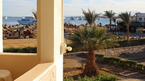 Un balcón con vistas a una playa, palmeras y barcos en el agua.
