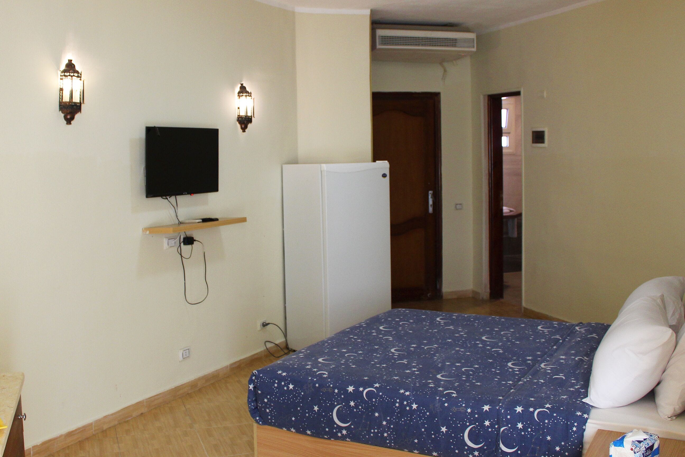 Un dormitorio con cama, televisor en la pared y refrigerador.