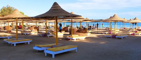 Een privéstrand, ligstoelen aan het strand, parasols, beachvolleybal