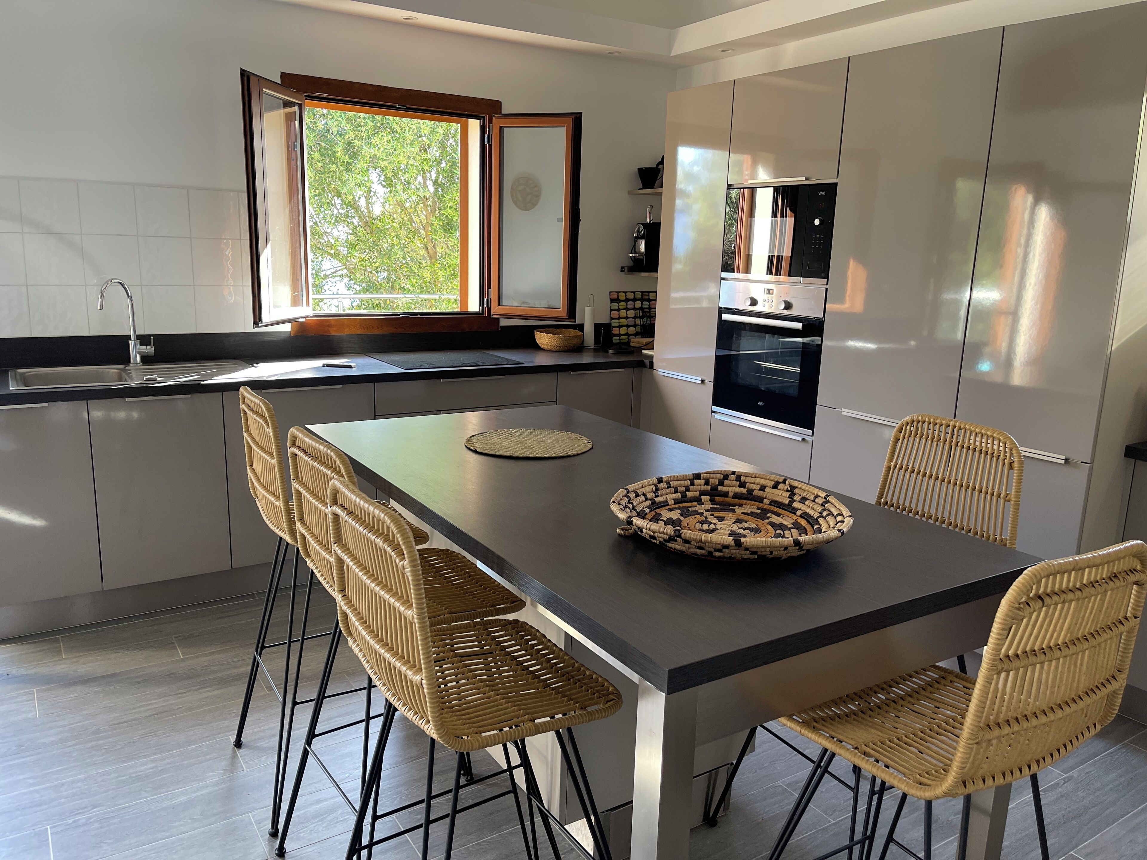 Une cuisine moderne dotée d’un îlot central, d’appareils électroménagers intégrés et d’une grande fenêtre.