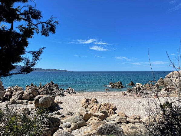Ein felsiger Strand mit klarem, blauem Wasser und sanften Hügeln in der Ferne.