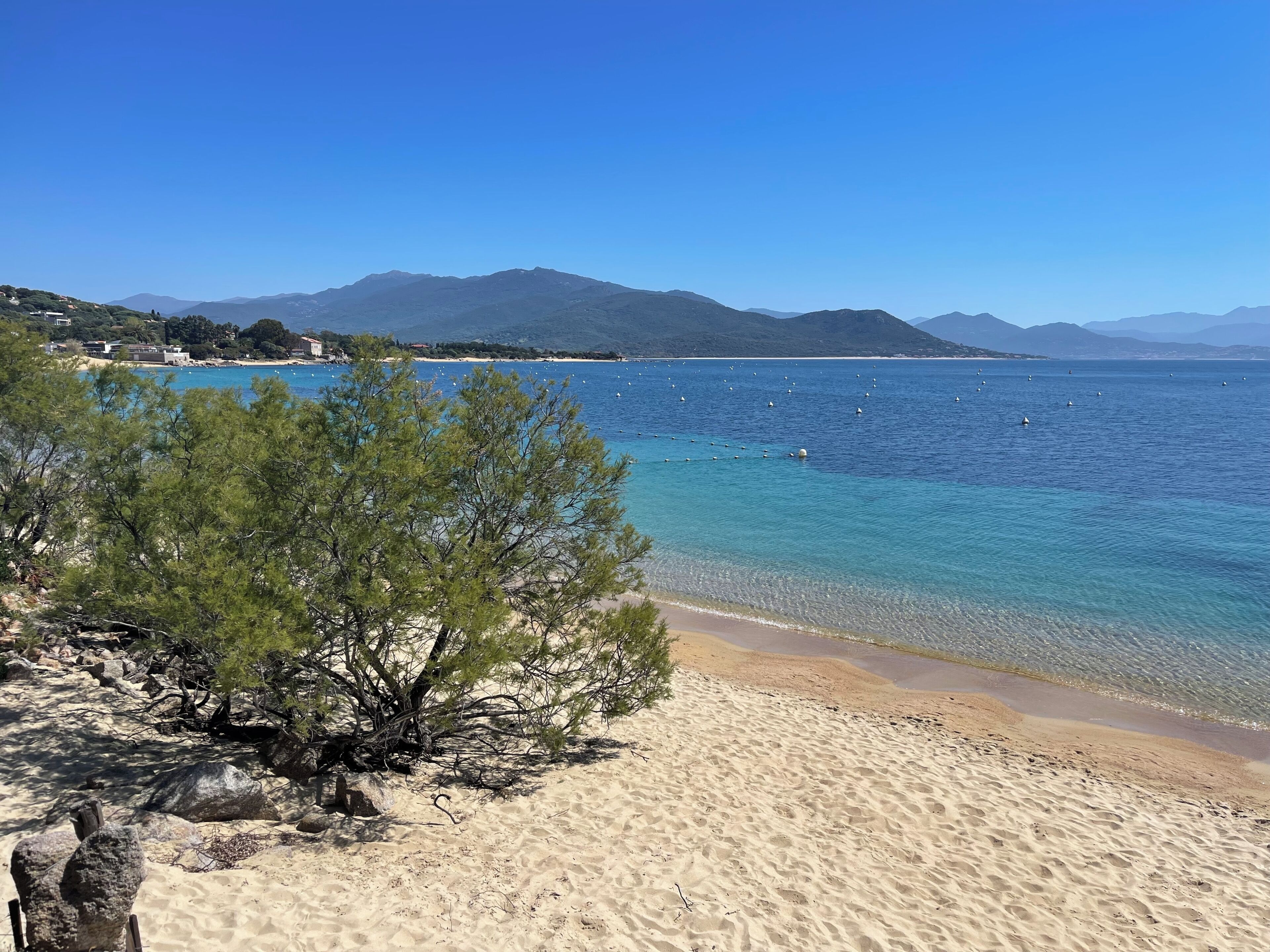 Une plage à l’eau claire, avec un rivage sablonneux et des montagnes qui se dessinent à l’horizon.