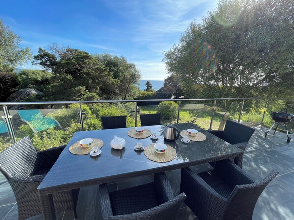 A table set outdoors with a view of the sea and greenery. - Villa Santa (Olmeto)