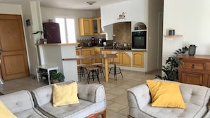A living room with two grey sofas and yellow cushions, a wooden coffee table, and a kitchen in the background with yellow cabinets and a stove.