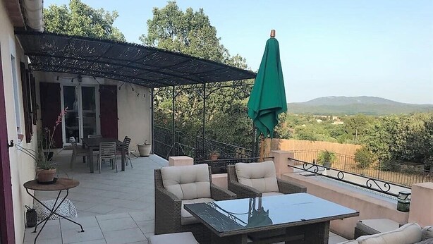 An outdoor patio with wicker furniture, a glass table, and a green umbrella.
