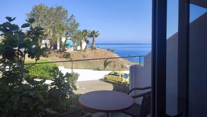 A balcony with a view of the sea, a yellow car, and some greenery.
