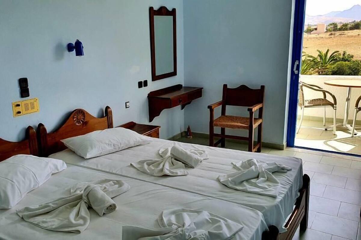 Een hotelkamer met twee bedden, een houten hoofdbord, een klein houten bureau, een stoel, een spiegel en uitzicht op de omgeving.