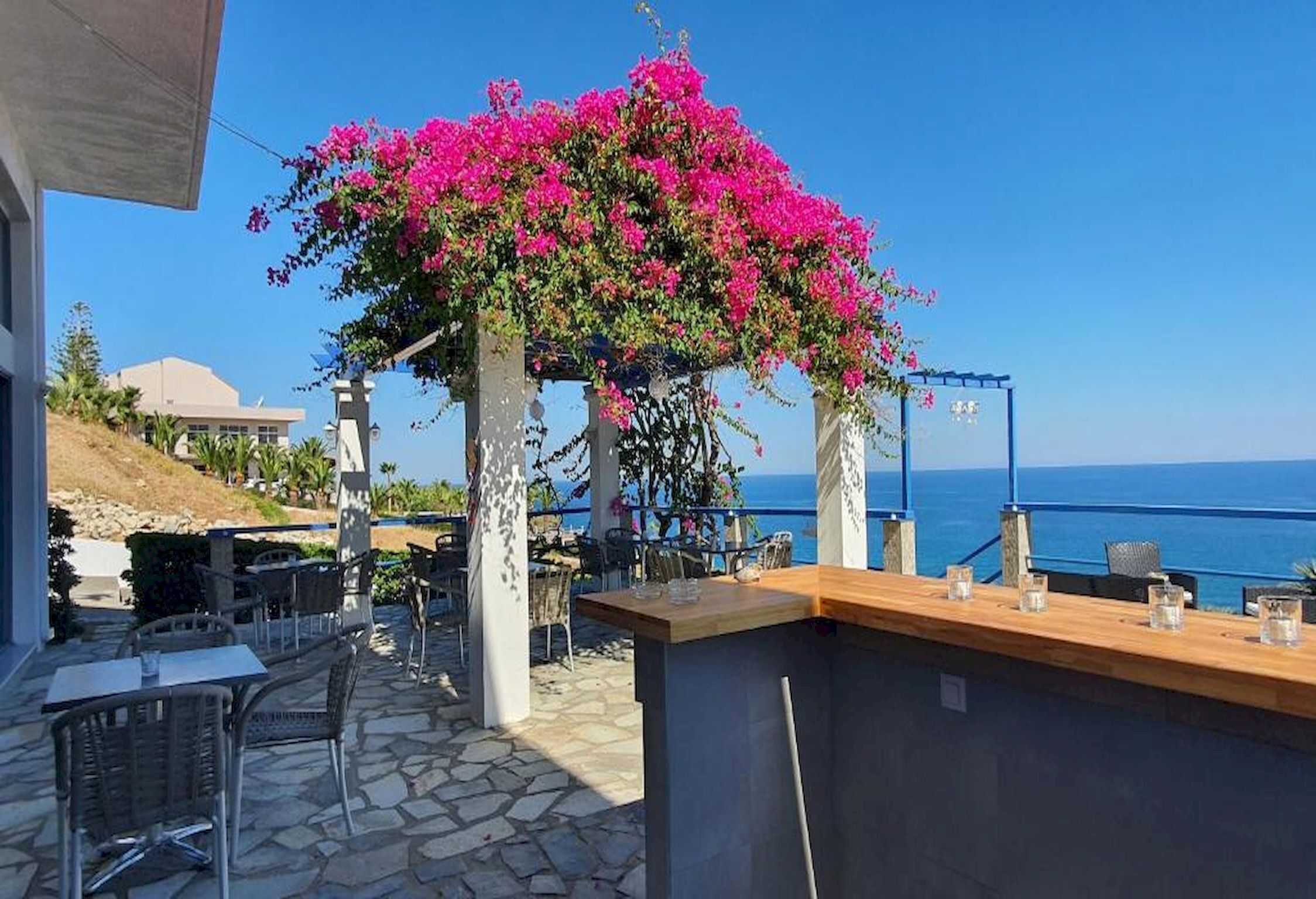 Un espace extérieur aménagé avec un sol en pierre, un bar en bois et une vue sur la mer.
