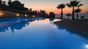 A serene pool area at dusk with calm water reflecting the sky and surrounding palm trees.