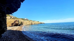 A coastal scene with a rocky beach, clear blue sea, and a building on a hillside.