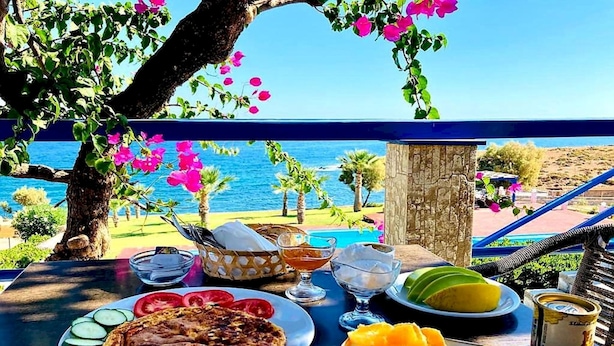 A table with food and drinks, overlooking a pool and the sea.