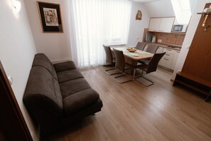 A modern living room with a sofa, dining table, and chairs. There is a kitchen area with cabinets and a microwave.