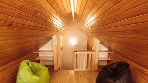 Un dormitorio en ático con listones de madera en el techo, una pequeña escalera de madera y dos pufs.