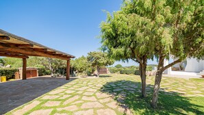 A stone patio with a pergola, a tree, and a white building in the background. - Villa Adele, sea view, pool, 700 meters from the beach (MONTE PETROSU)