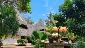 A tropical resort with thatched-roof buildings, a stone pathway, and outdoor seating under umbrellas. - Villa Mongoose Forest Dream Resort (Diani Beach)