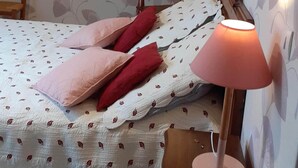 Un dormitorio con cama, almohadas, lámpara de noche, una silla y una pared con estampado floral.