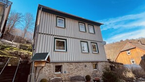 Un bâtiment à deux étages, avec une base en pierre et un revêtement métallique, doté d’une petite entrée et d’un banc à l’extérieur.