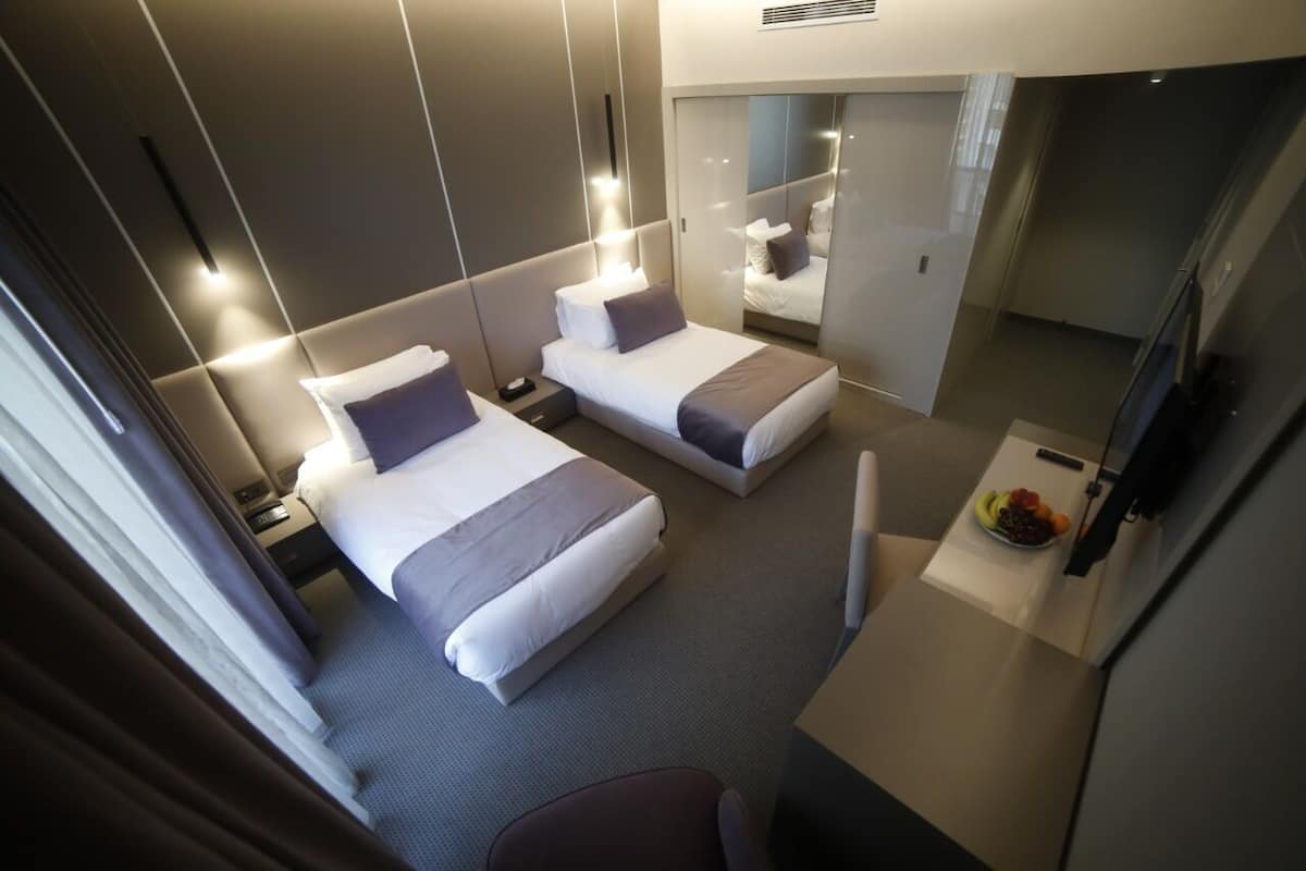 A hotel room with two beds, a small desk, a chair, and a fruit bowl on the side table.