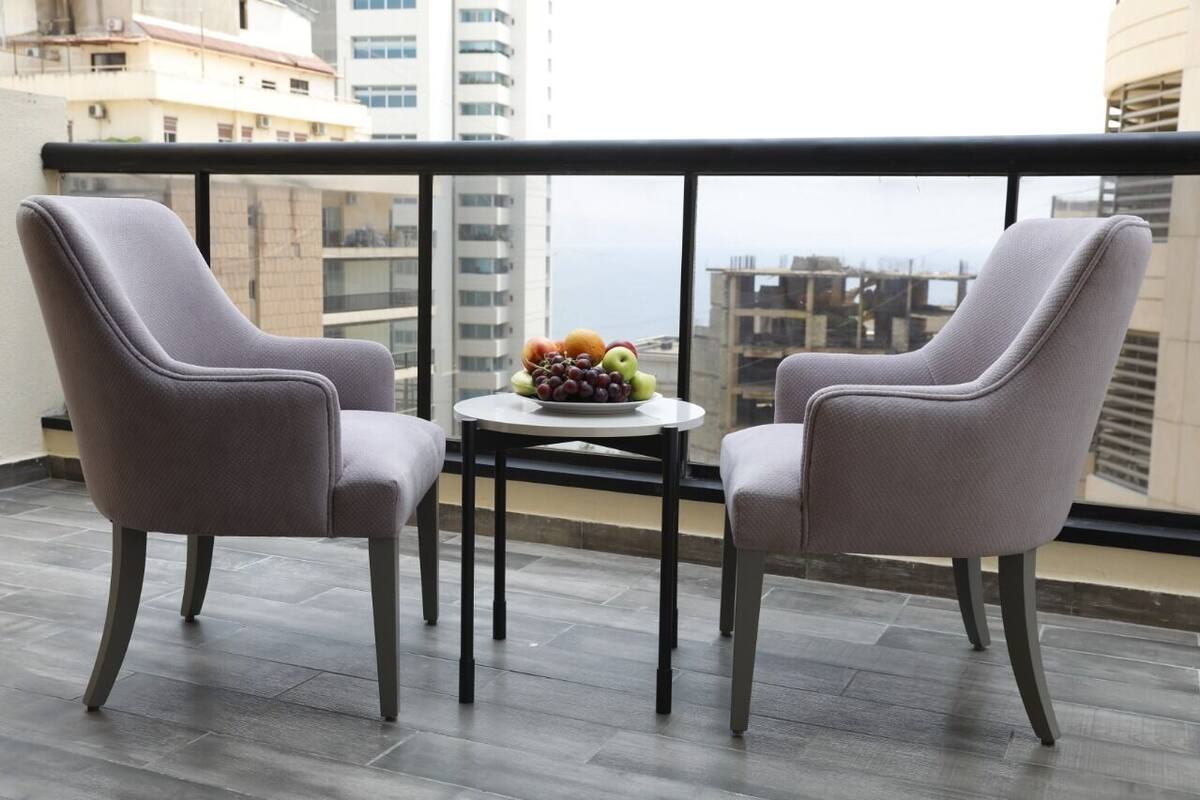 A balcony with two grey chairs, a small round table, and a fruit bowl.