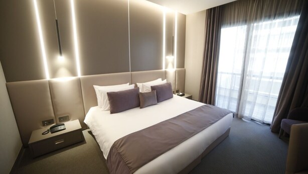 A hotel room with a large bed, bedside tables, a telephone, and a view of the outside through the window. - Rawsheh 51 (Beirut)