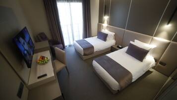 Habitación de hotel con dos camas, un escritorio con frutero, televisor y ventana con cortinas.