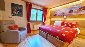 A cozy bedroom with a bed, a chair, a window with curtains, and a wall with framed pictures. - Casa Margherita (Challand-Saint-Anselme)