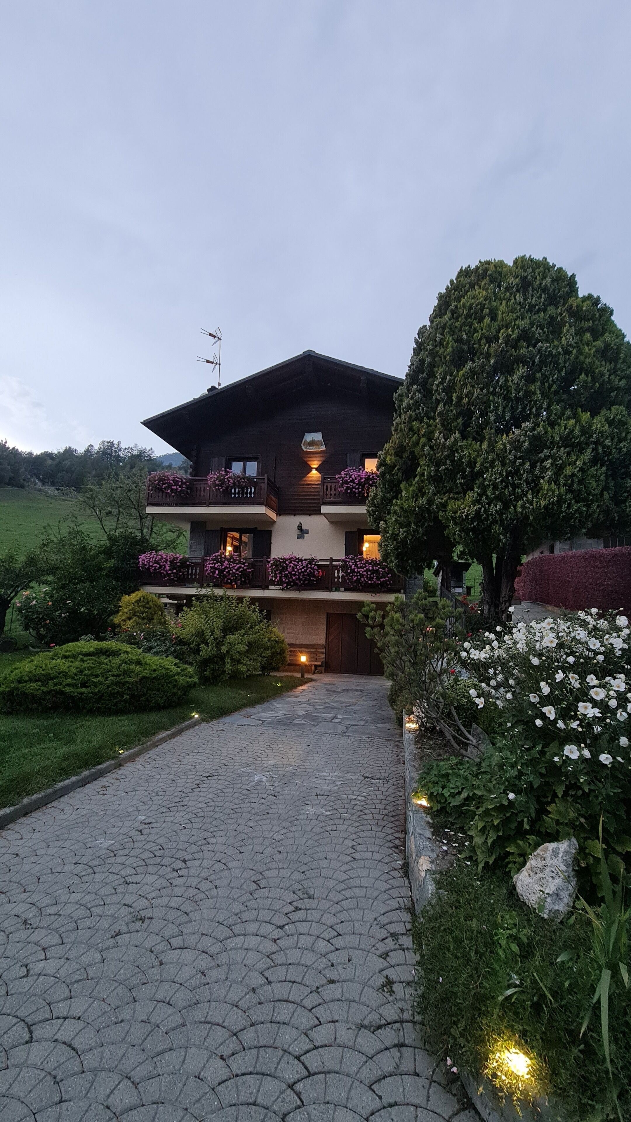 Un edificio a due piani con un balcone su ogni piano, circondato da giardini curati e un vialetto lastricato che conduce all'ingresso.