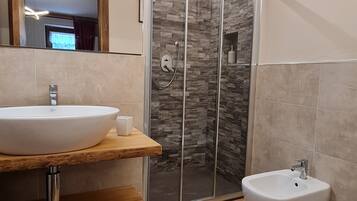 A modern bathroom with a large sink, a bidet, and a glass-enclosed shower.