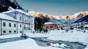 A snow-covered courtyard with a central fountain, buildings with snow-covered roofs, and mountains in the background. - Casa Margherita (Challand-Saint-Anselme)