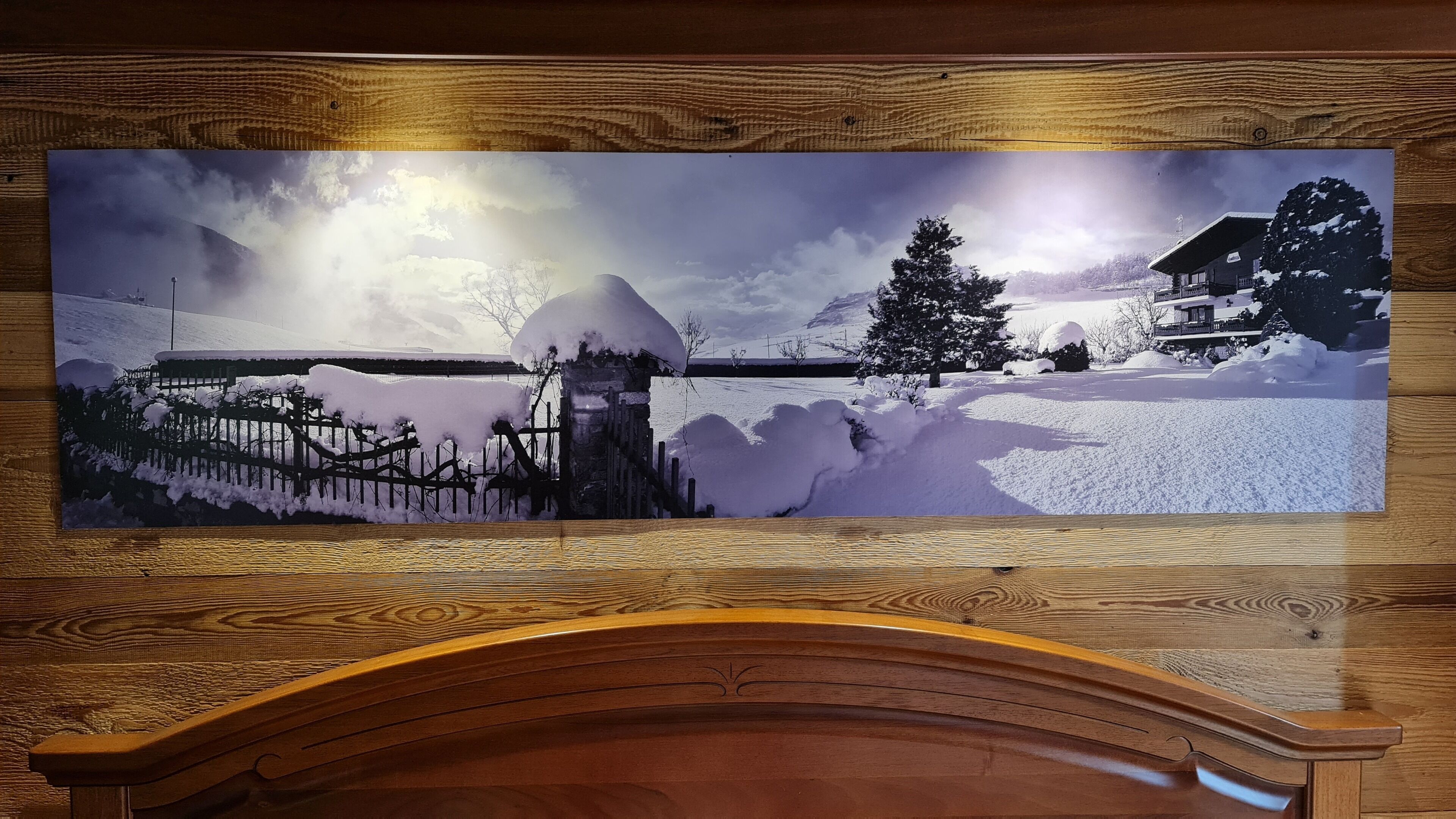 Panoramica di un paesaggio innevato con una recinzione di legno, una casa imbiancata dalla neve e un grande albero.