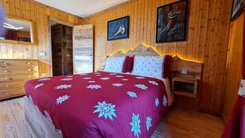 Quarto com painéis de madeira, uma cama, um aparador e duas pinturas nas paredes.