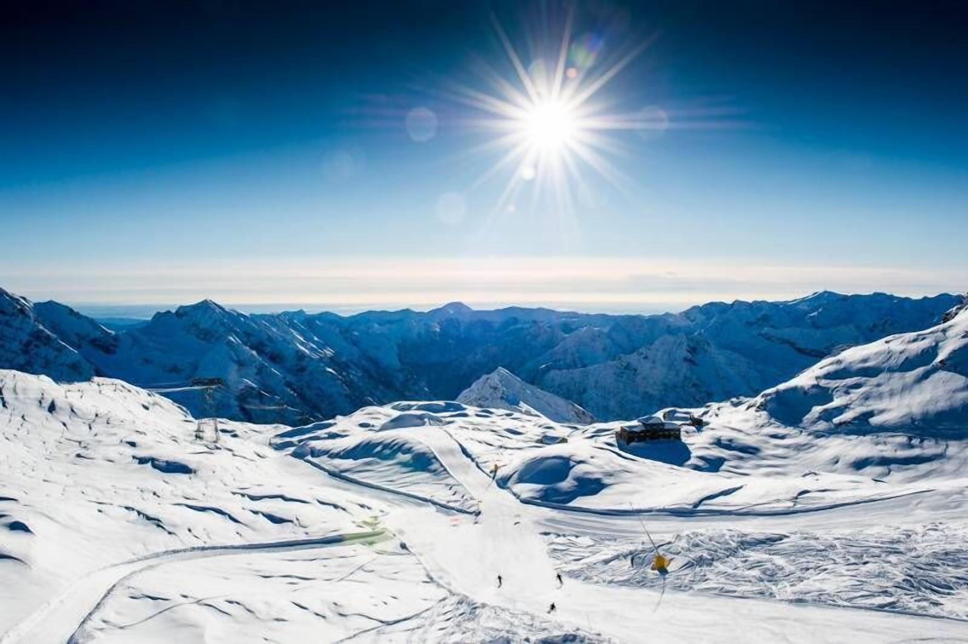 A snow-covered mountain landscape with a clear sky and a bright sun.