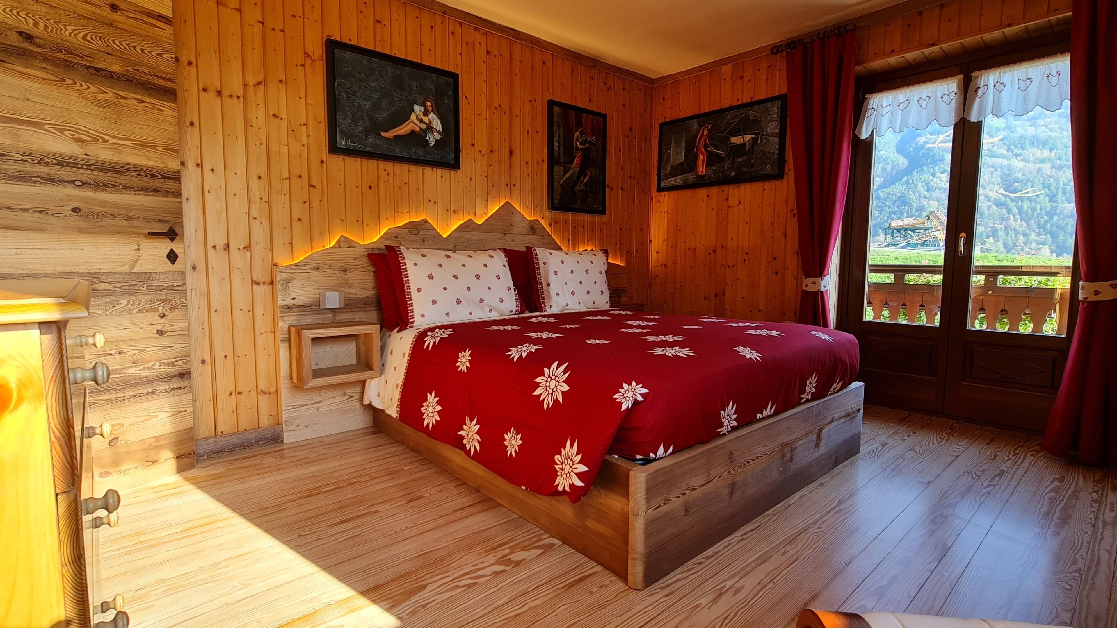 A wooden room with a bed, a nightstand, and a window with a view of greenery.