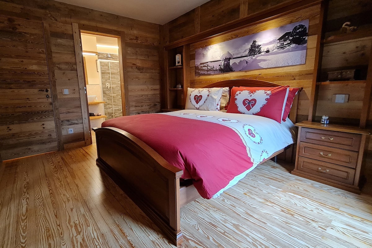 A wooden room with a bed, wooden floors, a painting on the wall, and a wooden cabinet.