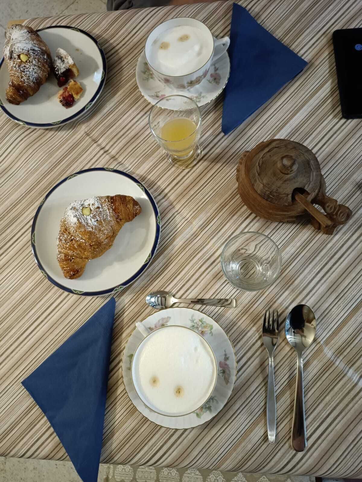 A table with croissants, a cup of coffee, a glass of juice, and a teapot.