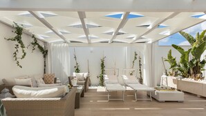 Un espace intérieur spacieux, aménagé avec des meubles en osier, des coussins blancs et des plantes en pot.