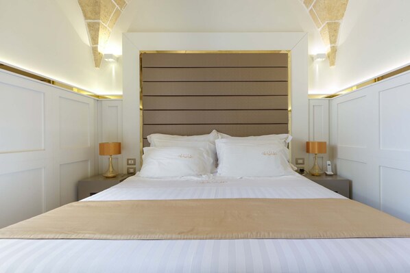 Una cama bien hecha con ropa blanca y un plaid color beige, flanqueada por dos mesitas de noche con lámparas, en una habitación con un diseño moderno y limpio.