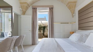 Une chambre dotée d’un grand lit, d’un bureau avec des chaises et d’une vue sur un espace extérieur, accessible par une porte ouverte.