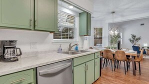 A modern kitchen with green cabinets, a dishwasher, and a coffee maker. There is a dining area with a table and chairs. - Restful Escape near Savannah (Richmond Hill)
