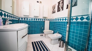 Un baño con lavamanos blanco, dos inodoros, un bidé y una zona de ducha.
