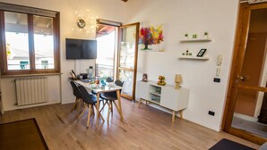 Un coin repas avec une table et des chaises, un téléviseur fixé au mur et une fenêtre donnant sur l’extérieur.