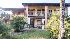 Un bâtiment à deux étages doté d’un balcon, d’une terrasse avec des chaises et de palmiers.