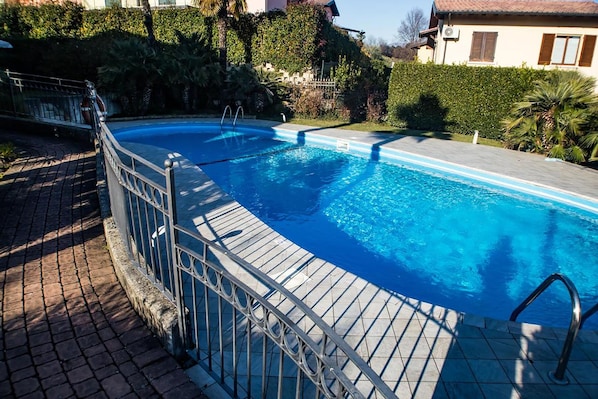 Una piscina con barandilla metálica, rodeada por un camino pavimentado y abundante vegetación.