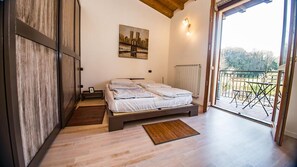 Un dormitorio con cama, piso de madera, un cuadro en la pared y un balcón con vistas.