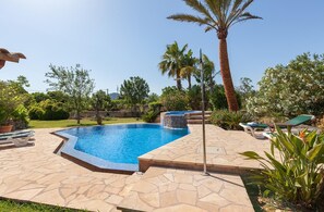 Una piscina con solárium de piedra, rodeada de palmeras y plantas diversas.